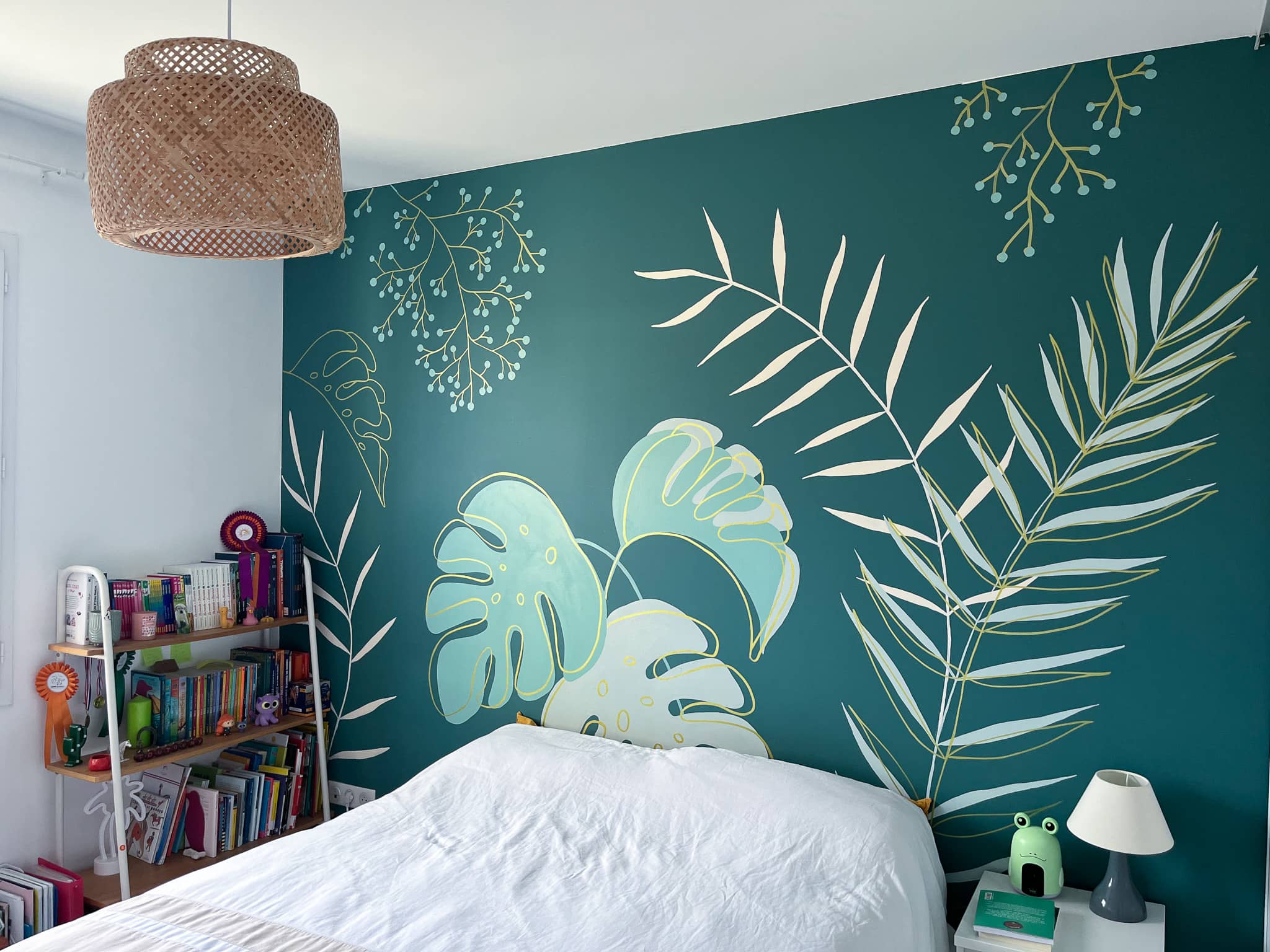 Fresque murale végétale en tête de lit dans une chambre d'adolescente : motifs botaniques sur fond vert canard pour une ambiance nature et apaisante. La décoration murale sur mesure devient le cœur de la pièce.