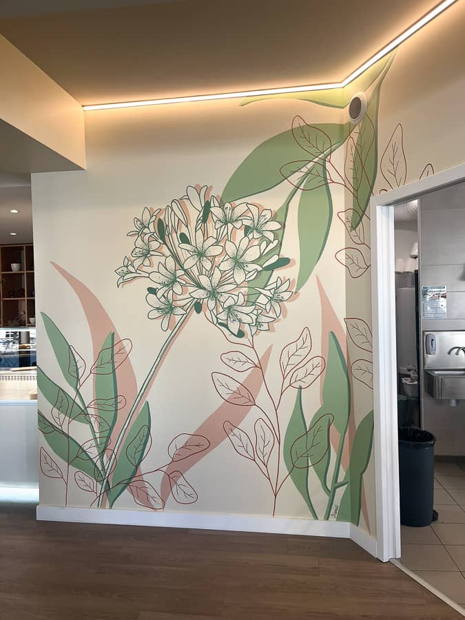 Fresque murale restaurant peinte sur mesure : agapanthe et feuillages en rose poudré et vert sauge sur fond blanc crème. Une décoration murale végétale qui crée une identité visuelle forte et une ambiance chaleureuse pour vos clients.